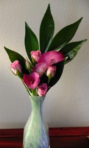 Pink spray roses and pink mini calla lilies pop against a fan of laurel.