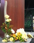 Yellow Toscana roses, magnolia, cream lisianthus, bronze cremone mums, yellow spray roses, white hydrangea, and white mums draw attention to a slender speaker's podium.