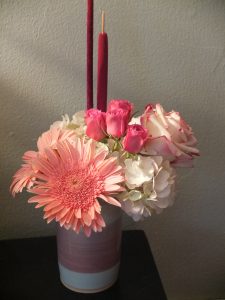 Blush pink hydrangea, hot pink spray roses, baby pink gerbera daisies, magenta cattails, and a bicolour pink rose in a cylinder vase are the perfect touch for a beauty salon's counter.